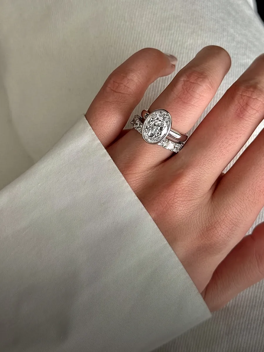 A hand wearing a silver engagement ring with an oval diamond and a wedding band.