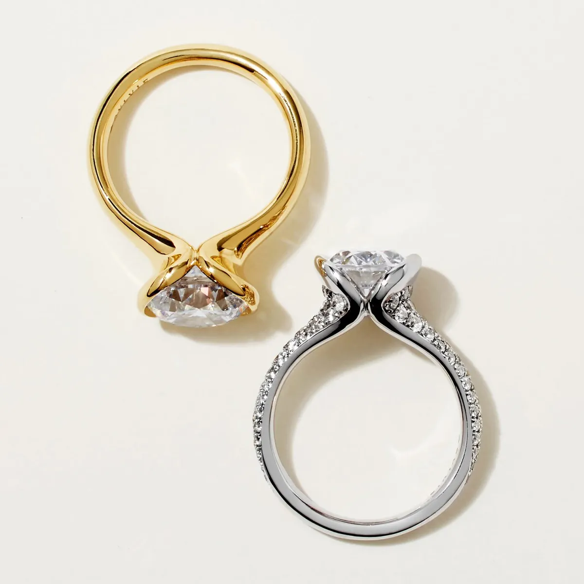 Two engagement rings: one gold with a solitaire diamond, the other silver with a diamond and smaller stones on the band.