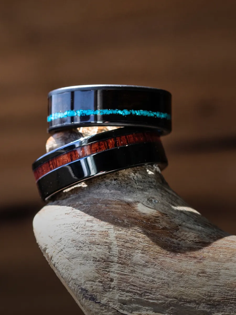 Two black rings with turquoise and wood inlays displayed on a wooden surface.