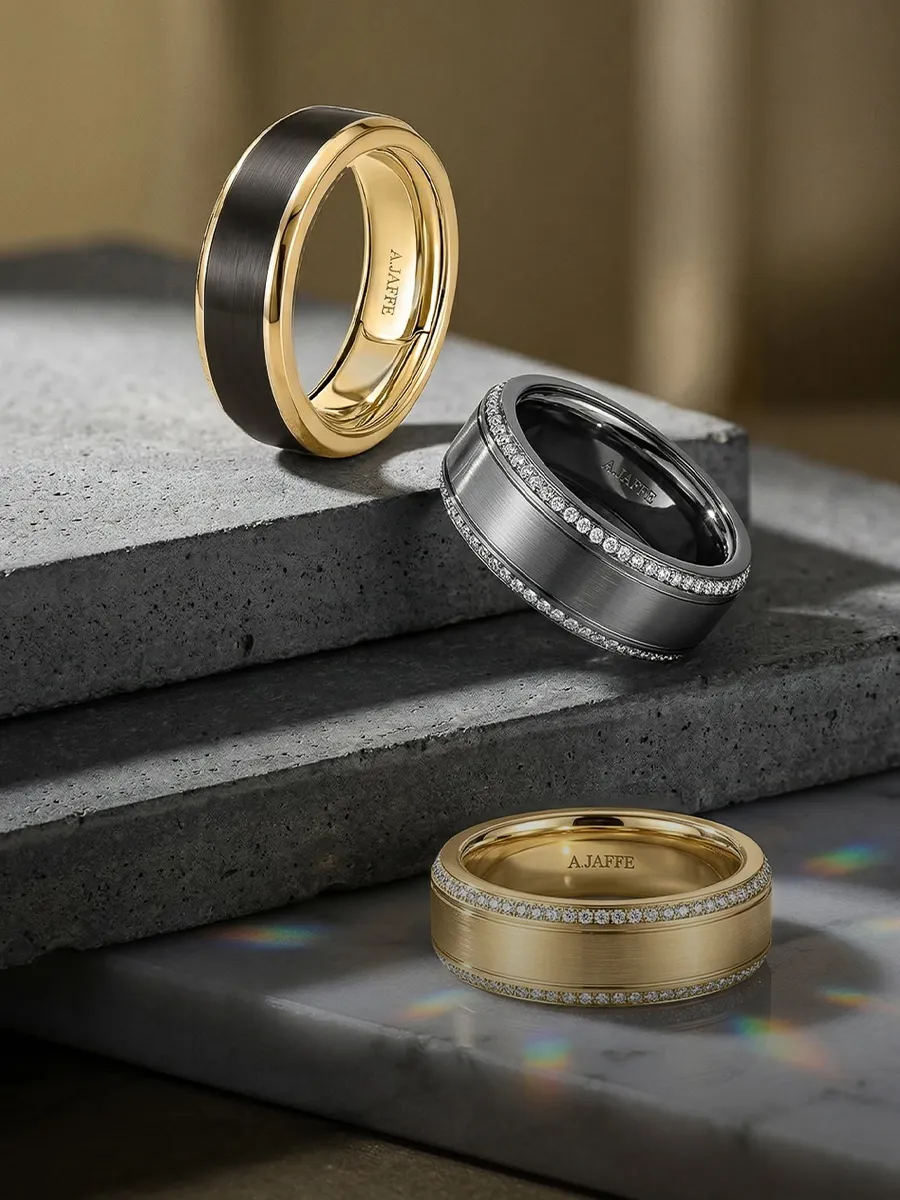 Three elegant wedding bands displayed on stone surfaces, featuring gold and silver tones with diamond accents.