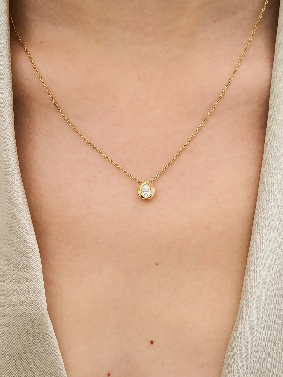 A gold necklace with a teardrop-shaped diamond pendant on a person's neck.