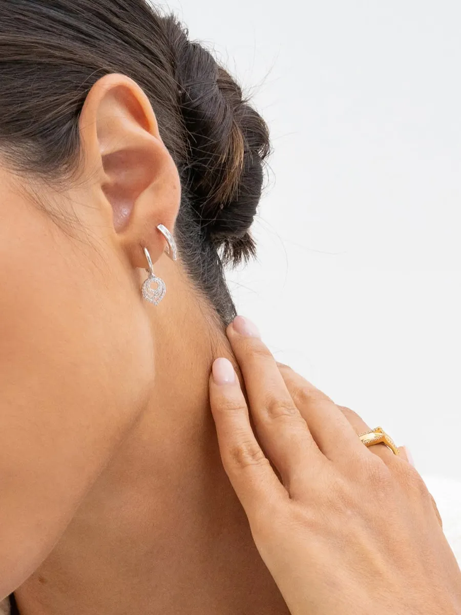 A person wearing silver hoop earrings and a gold ring, touching their neck.