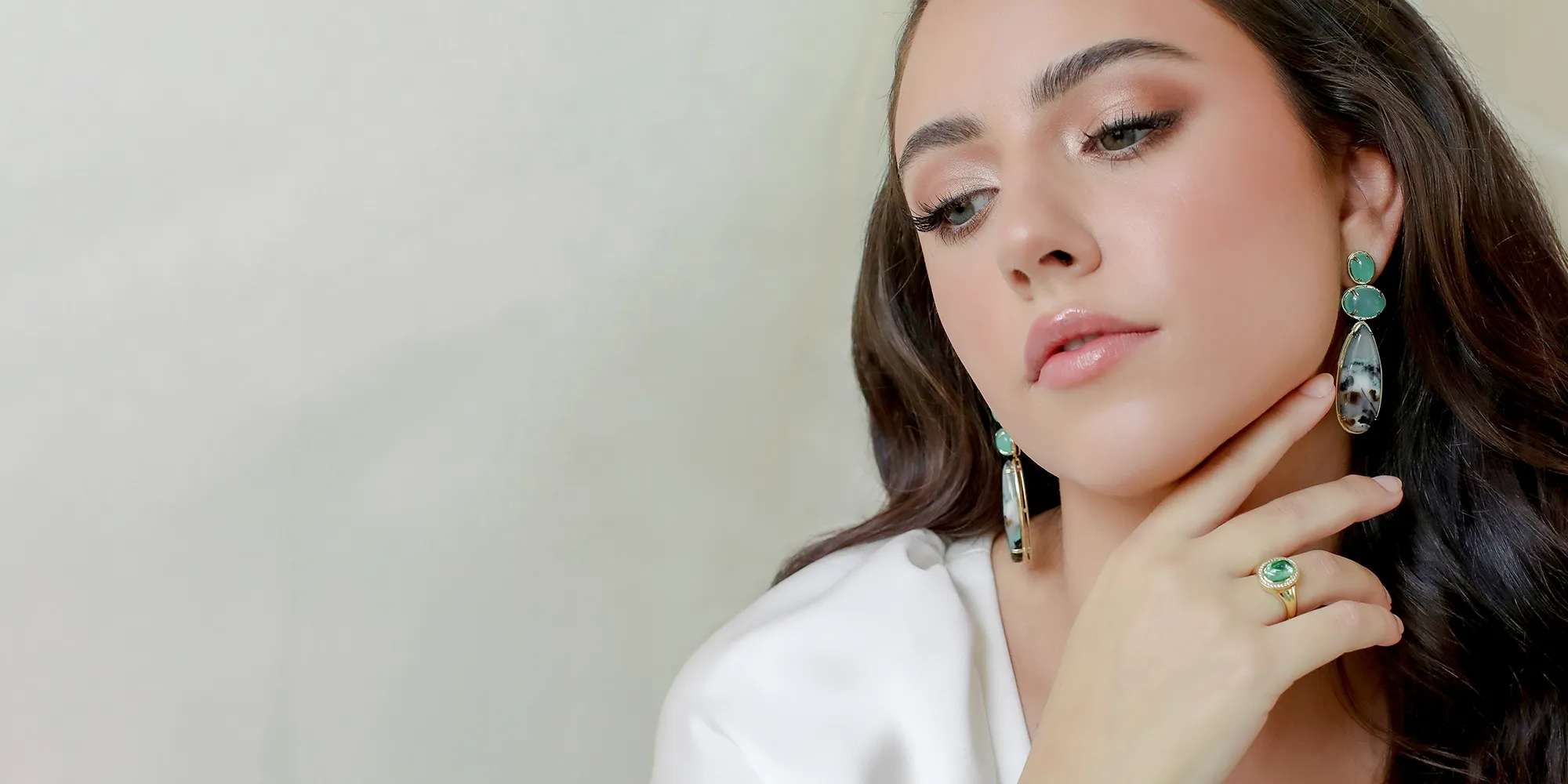 A woman wearing turquoise and spotted earrings, with a matching ring, in a white blouse.