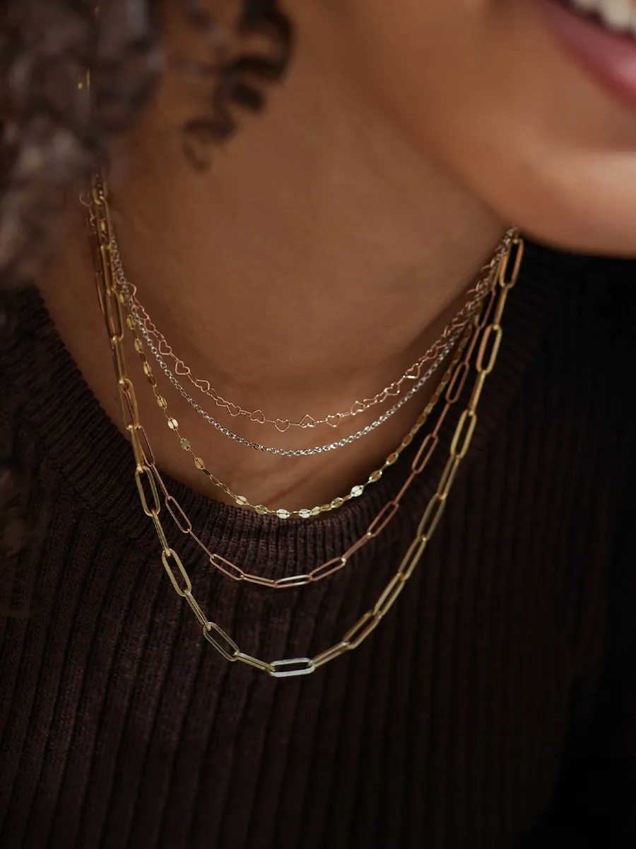 Layered gold and silver chains on a person wearing a dark ribbed sweater.