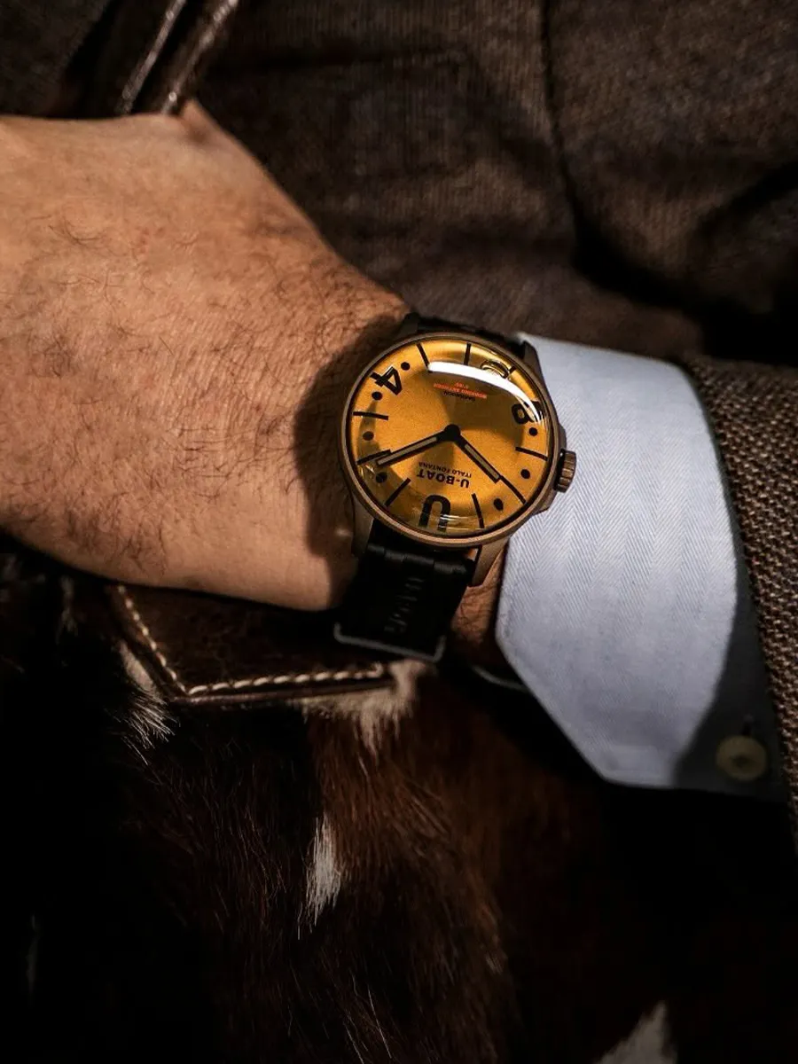 Gold watch with white face, gold numerals, and a gold bracelet on a soft cushion.
