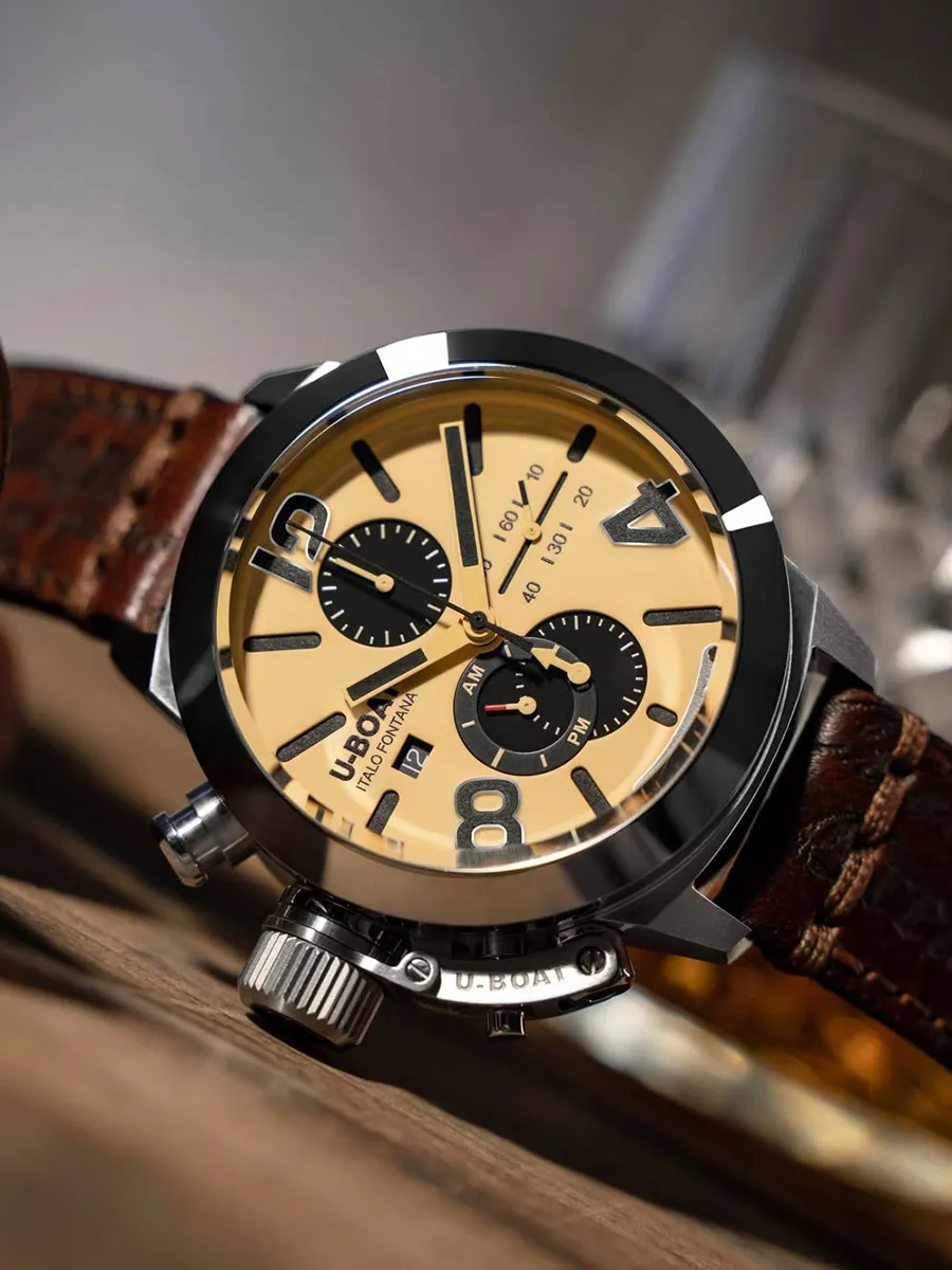 Brown leather strap watch with a beige dial and black accents on a wooden surface.