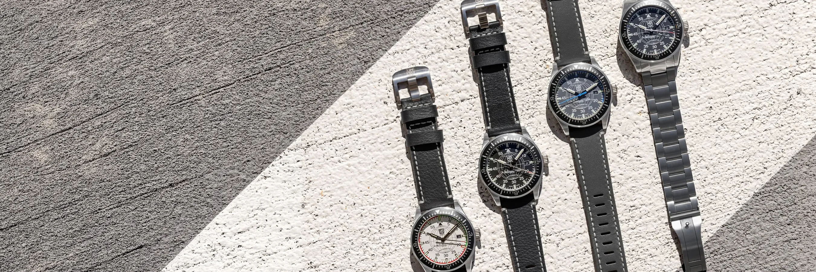 Four Luminox watches with black and gray straps displayed on a textured surface.