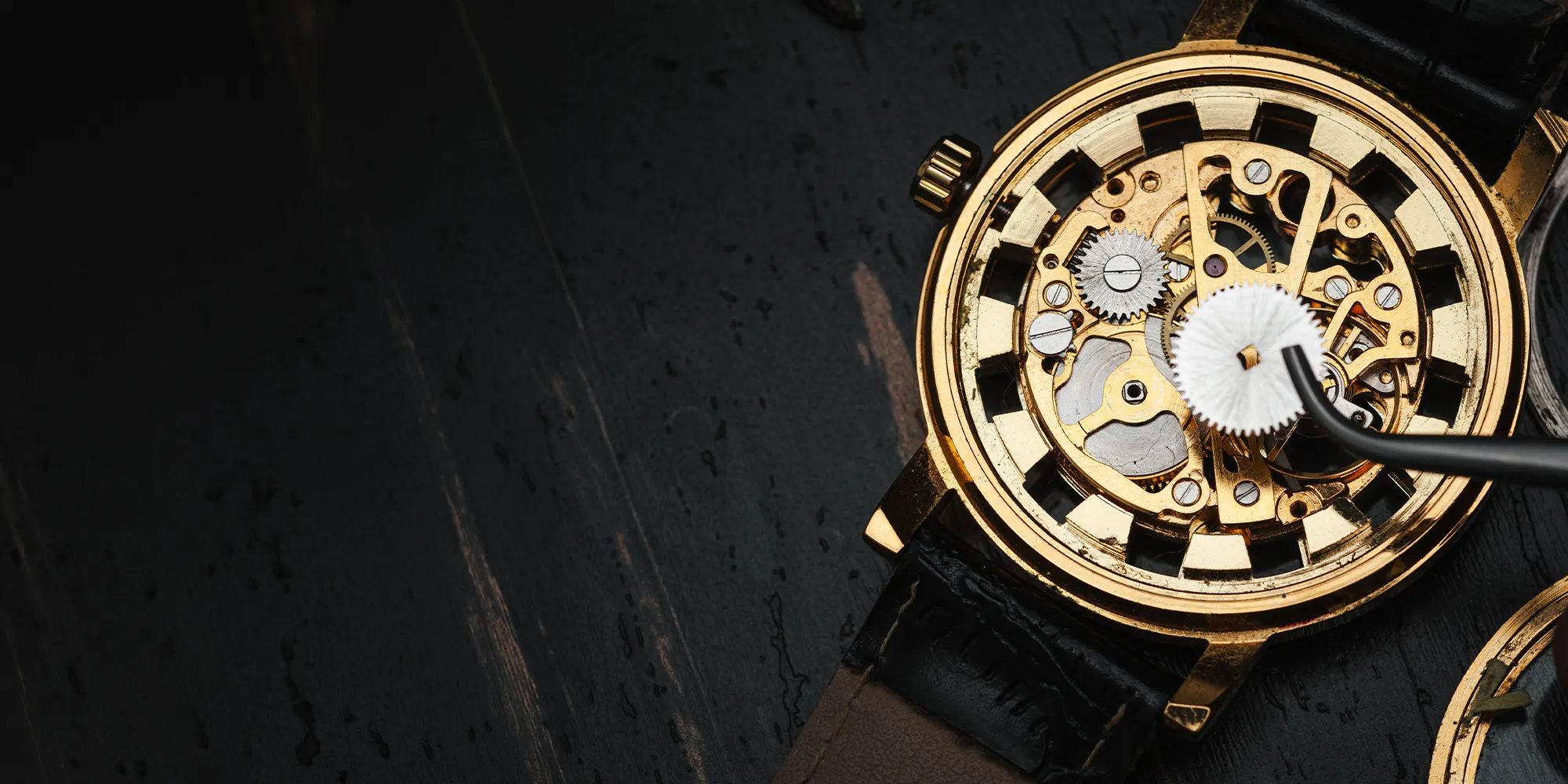 A close-up of a gold watch's intricate internal gears being repaired with tweezers.