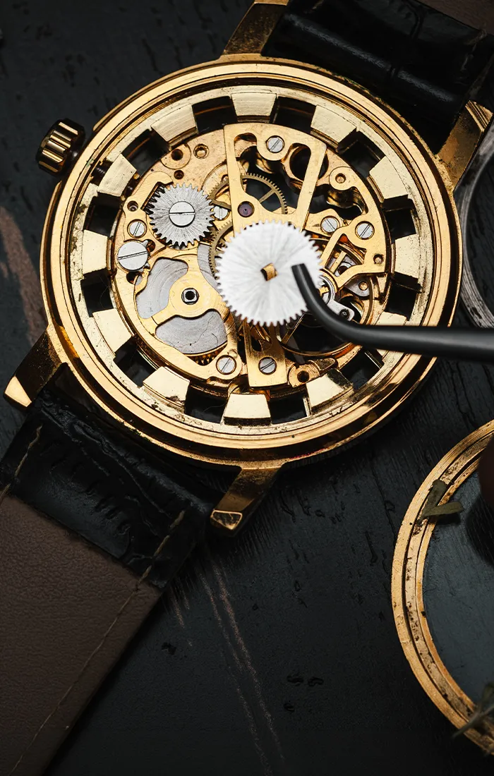 A close-up of a gold watch's intricate internal gears being repaired with tweezers.