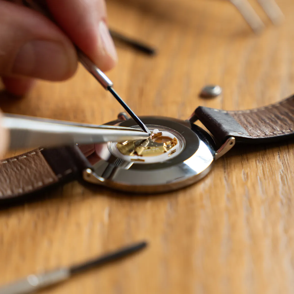 A watchmaker uses tools to repair a watch on a wooden table.