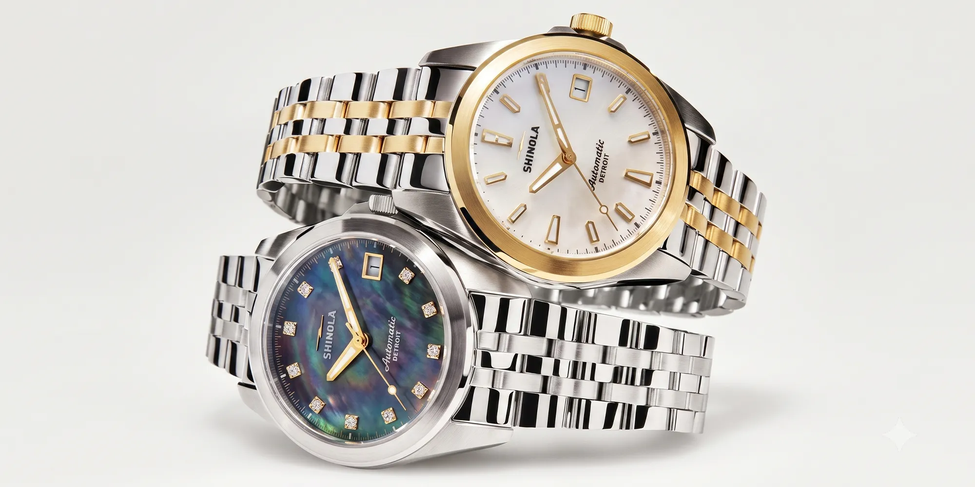 Two luxury watches with metal bands, one with a gold accent and white face, the other with a blue face and diamond markers.