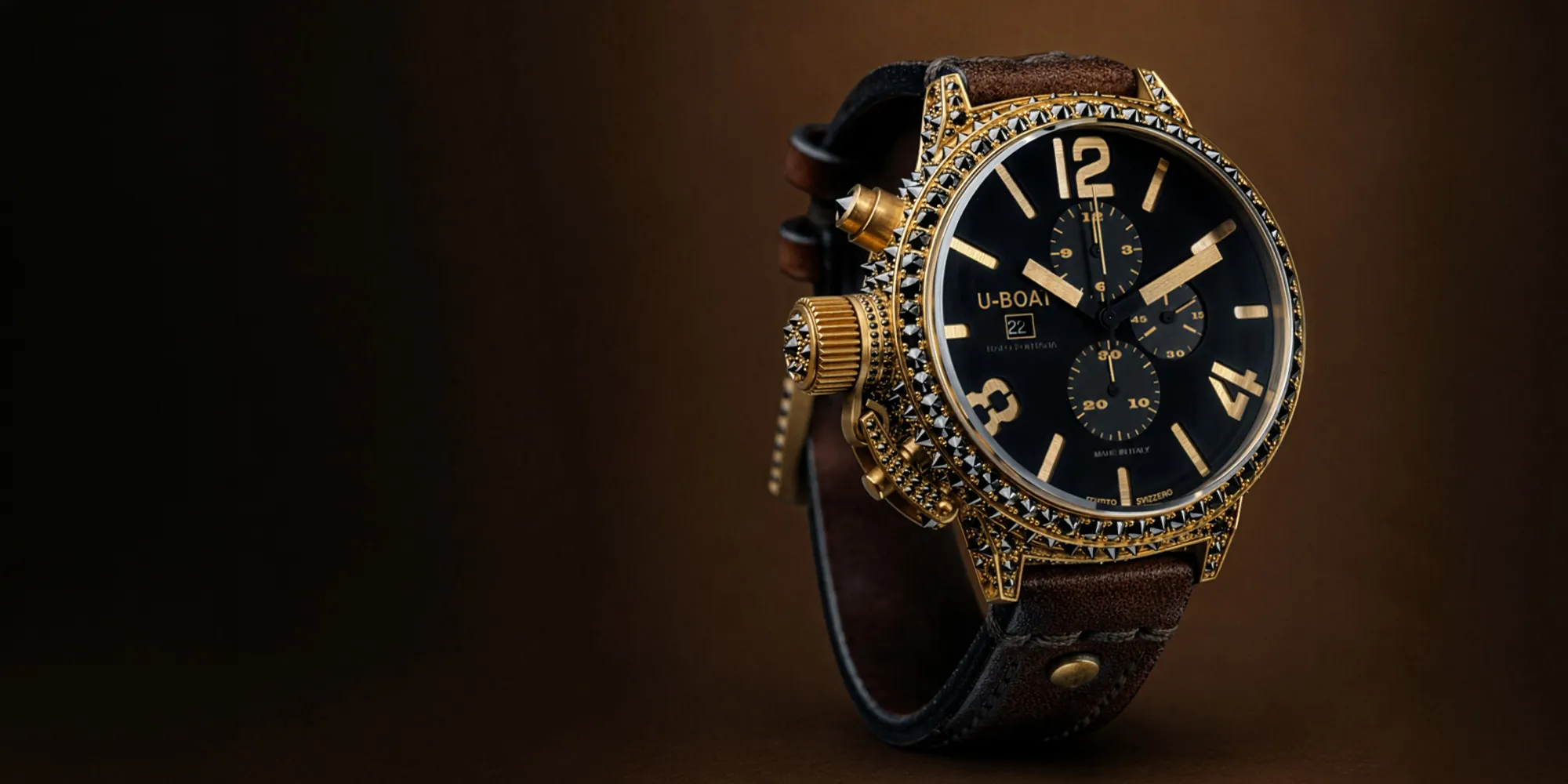 Luxurious gold and black watch with a studded bezel and brown leather strap on a brown background.
