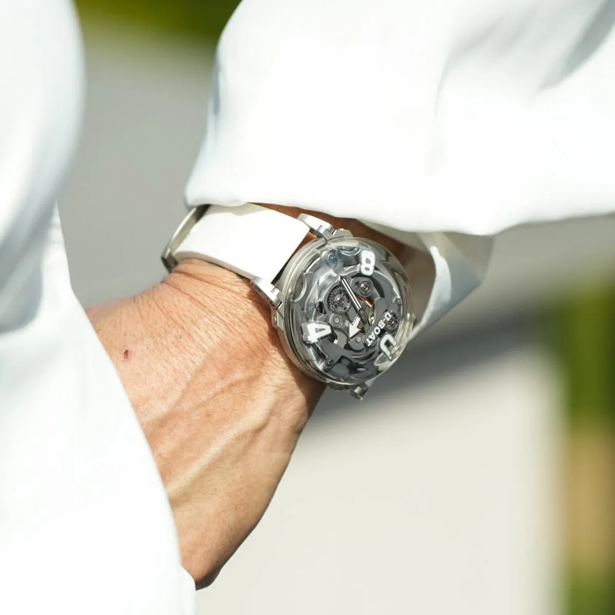A person wearing a white strap watch with a transparent dial showing intricate mechanics.