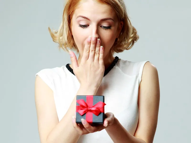 Surprised woman holding a gift box with a red ribbon. Click to shop WOWs at Holliday Jewelry in Klamath Falls.
