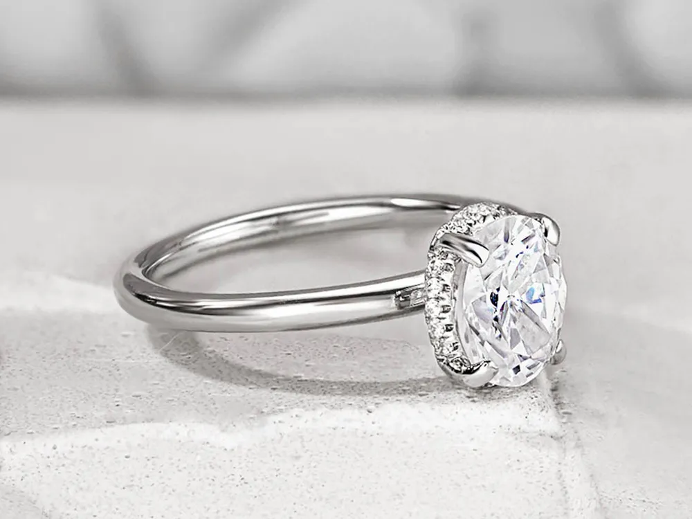 Elegant engagement ring featuring an oval diamond surrounded by smaller stones, set in a polished silver band.