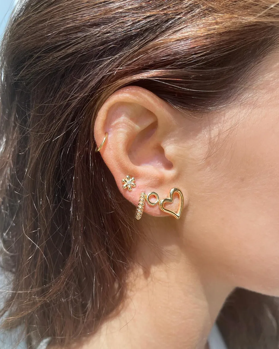 Gold earrings featuring a heart, flower, and spiral design worn by a model.