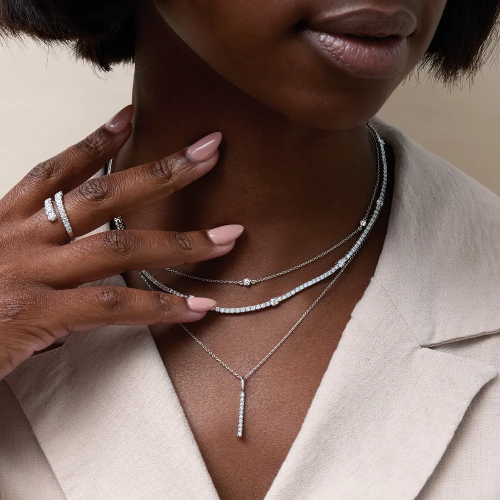 Close-up of a woman wearing layered silver necklaces and a ring, showcasing fine jewelry.