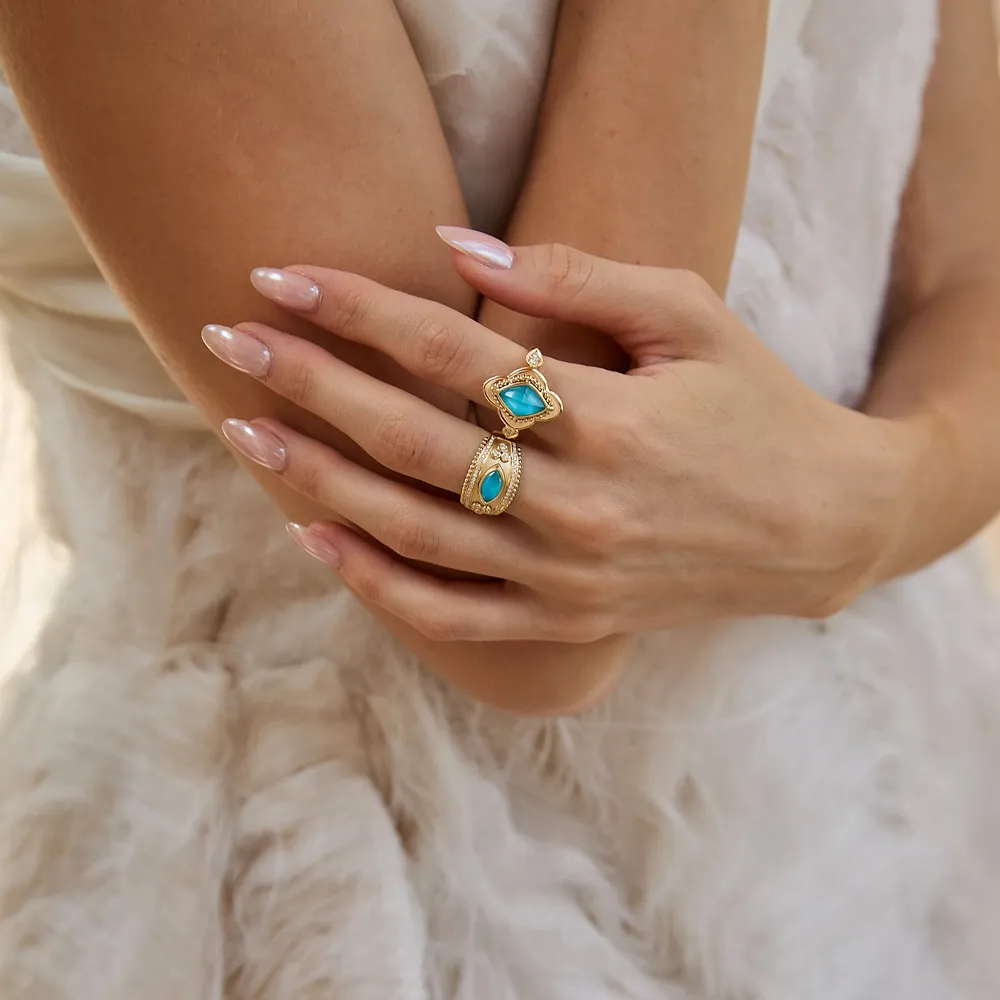 Elegant hands showcasing two gold rings with turquoise stones, perfect for fine jewelry lovers.