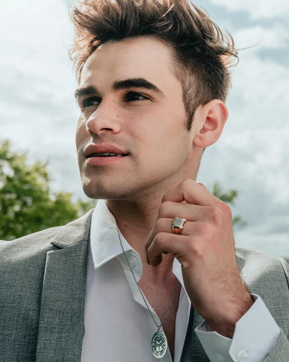 Stylish young man in a suit with a necklace and ring, promoting men's jewelry.