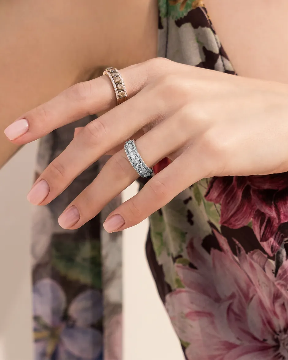 Two elegant rings on a hand, one gold with brown stones and the other silver with clear stones.