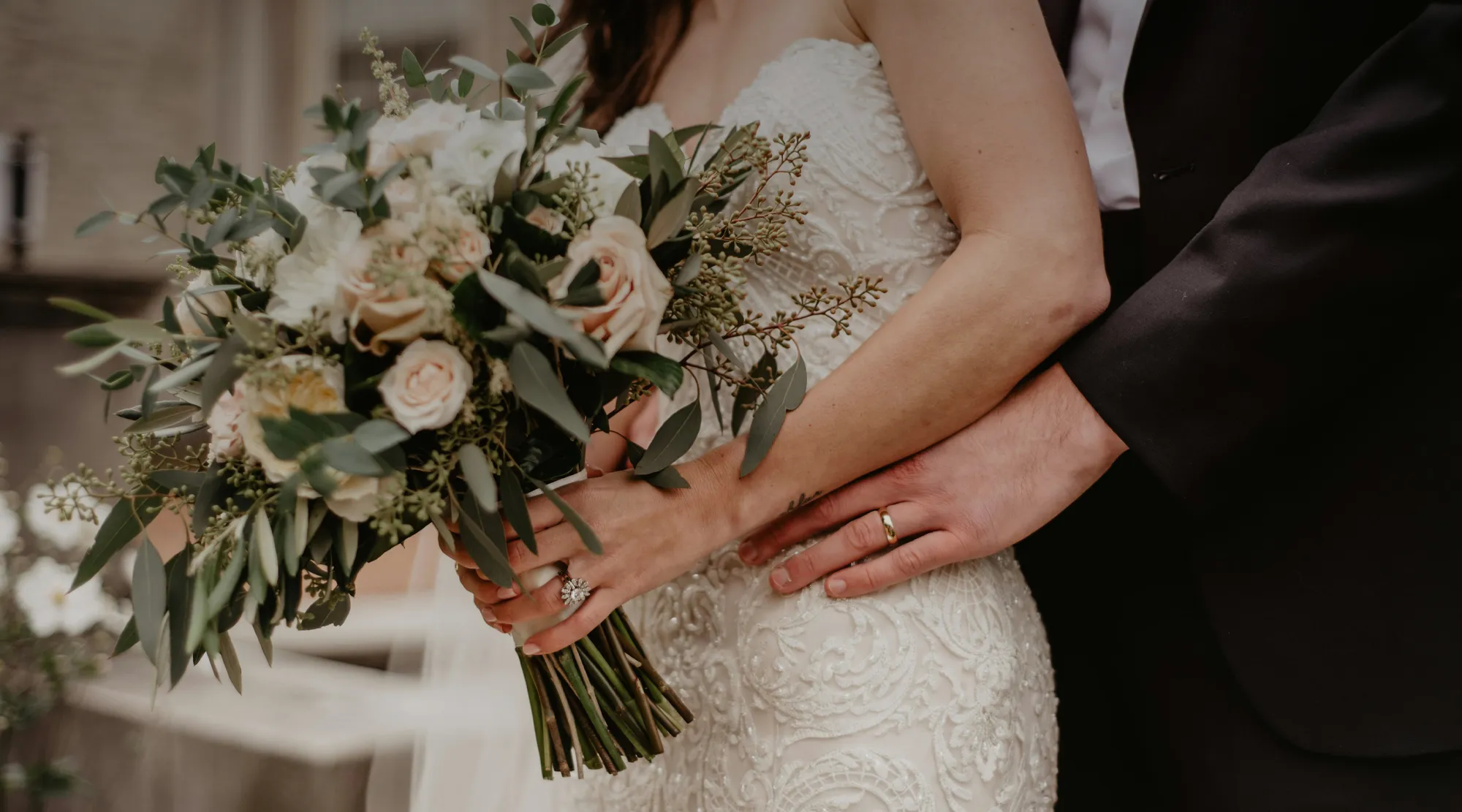 Bride holding a bouquet with groom's hand on her waist, showcasing love and elegance.