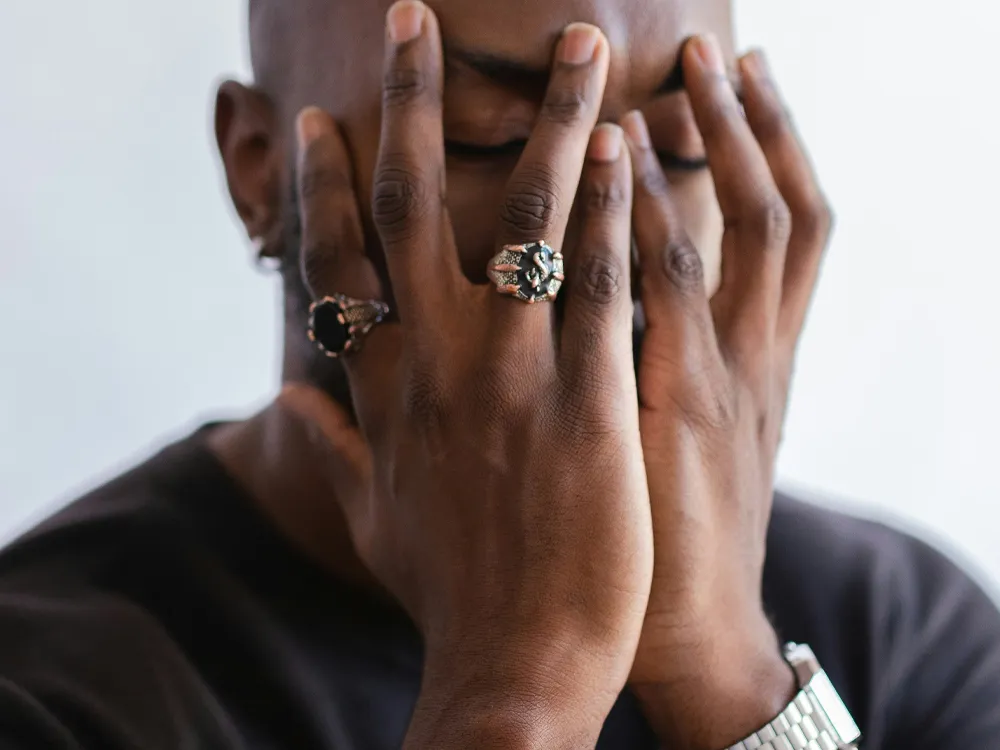 Man covering his face with hands, wearing rings, expressing emotion.