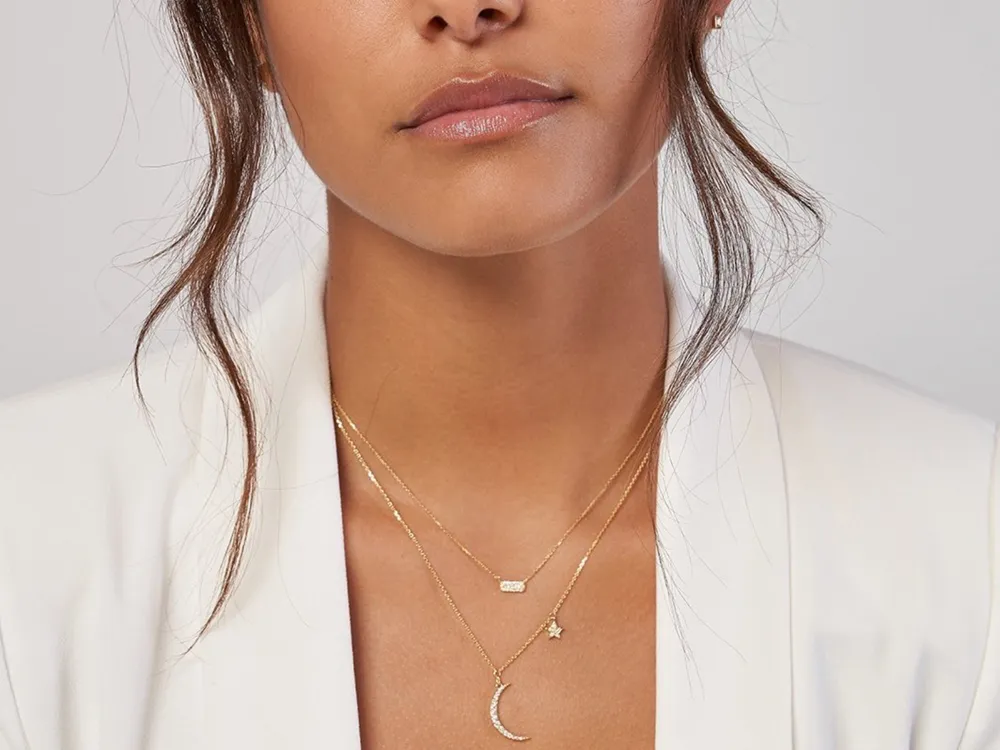 Model wearing layered gold necklaces featuring a crescent moon, star, and bar pendant.