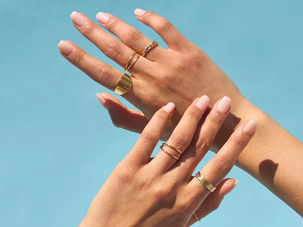 Two hands adorned with various gold rings against a blue background, showcasing elegant jewelry.