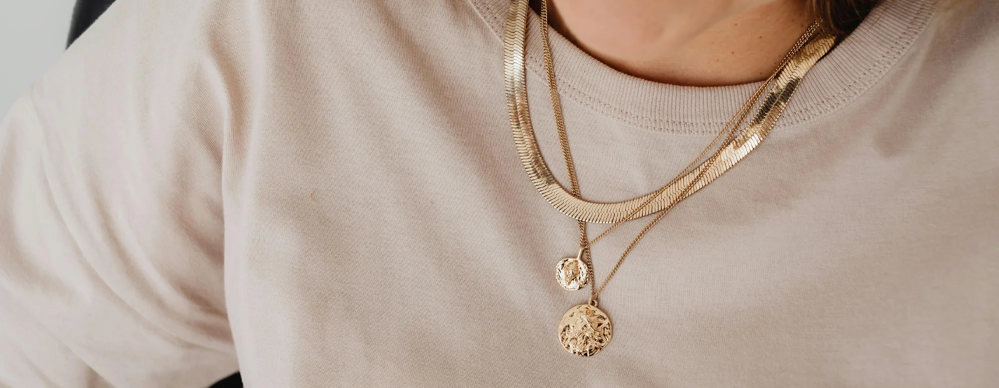 Close-up of layered gold necklaces worn over a light-colored shirt.