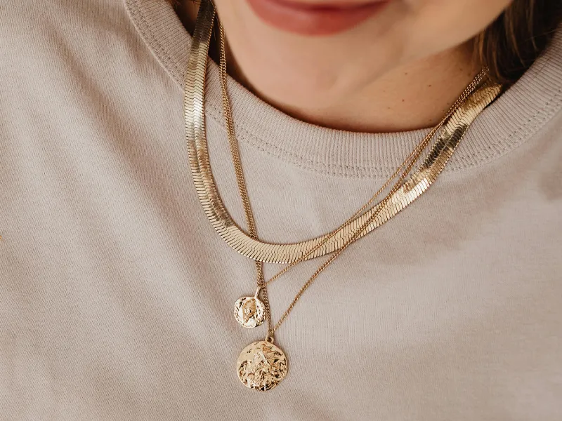 Close-up of layered gold necklaces worn over a light-colored shirt.