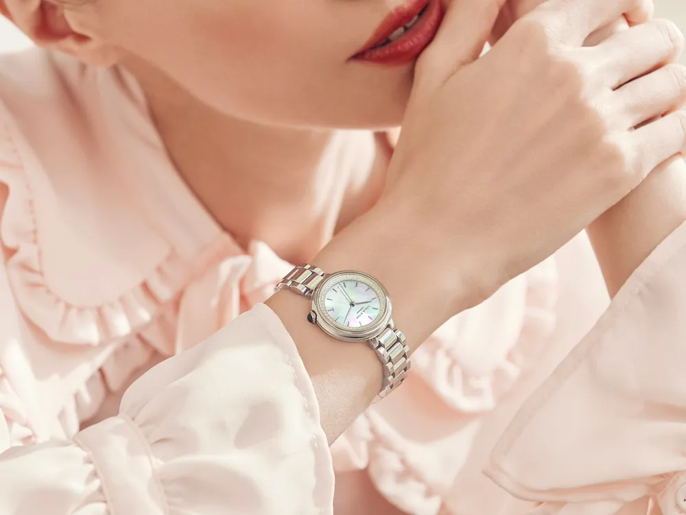 Close-up of a woman's wrist wearing a silver watch, showcasing its elegant design against a soft pink blouse.