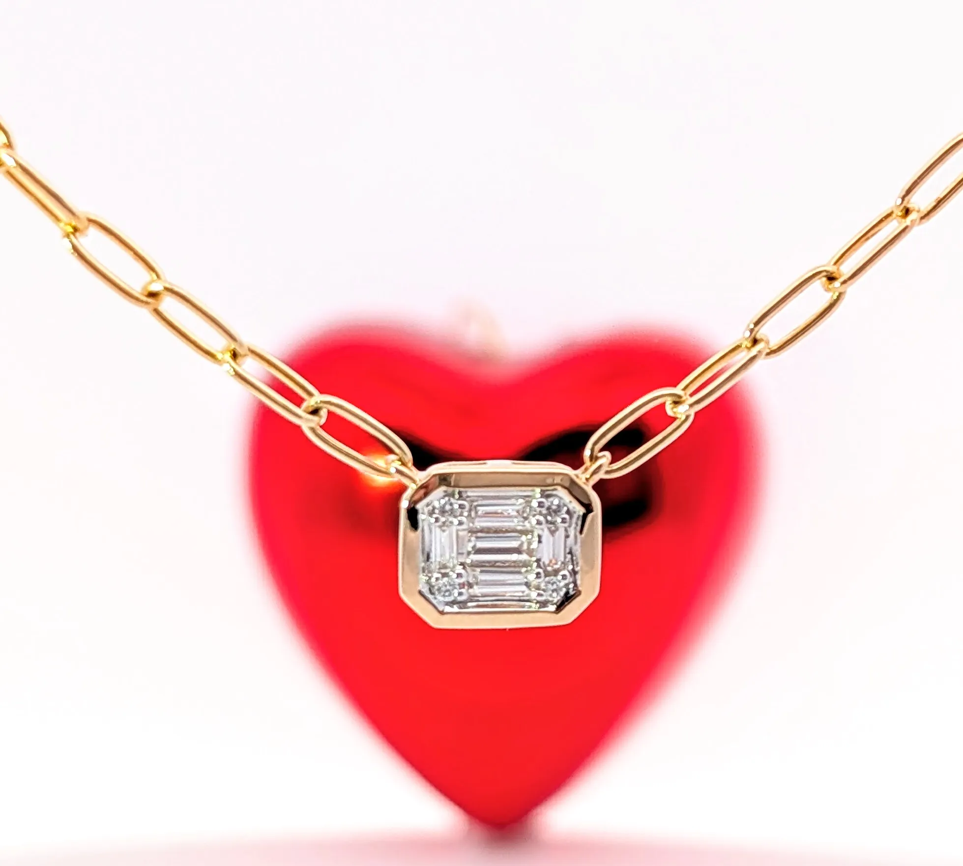 Elegant gold chain necklace with a diamond pendant, set against a red heart background. Visit Holly McHone Jewelers.