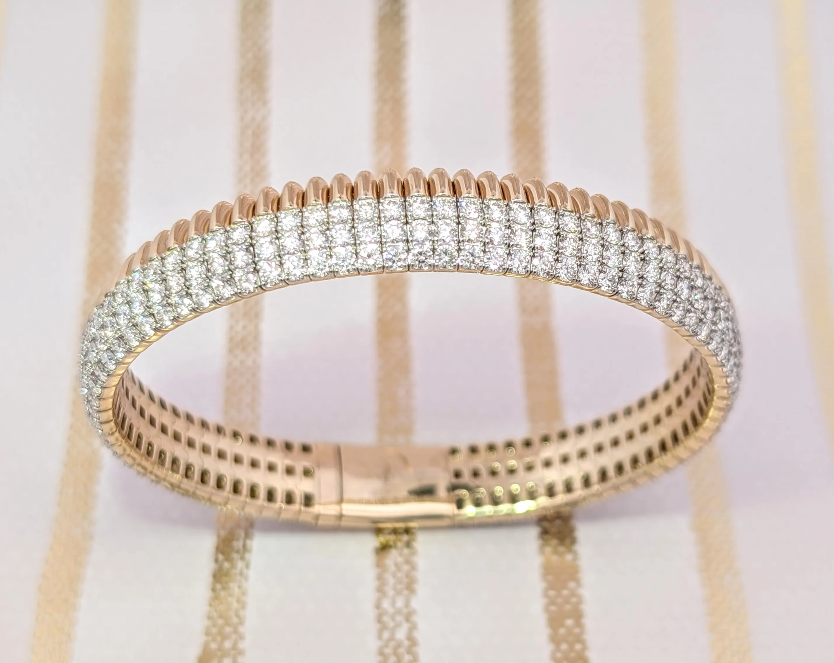 A gold bracelet with rows of sparkling diamonds on a striped background.