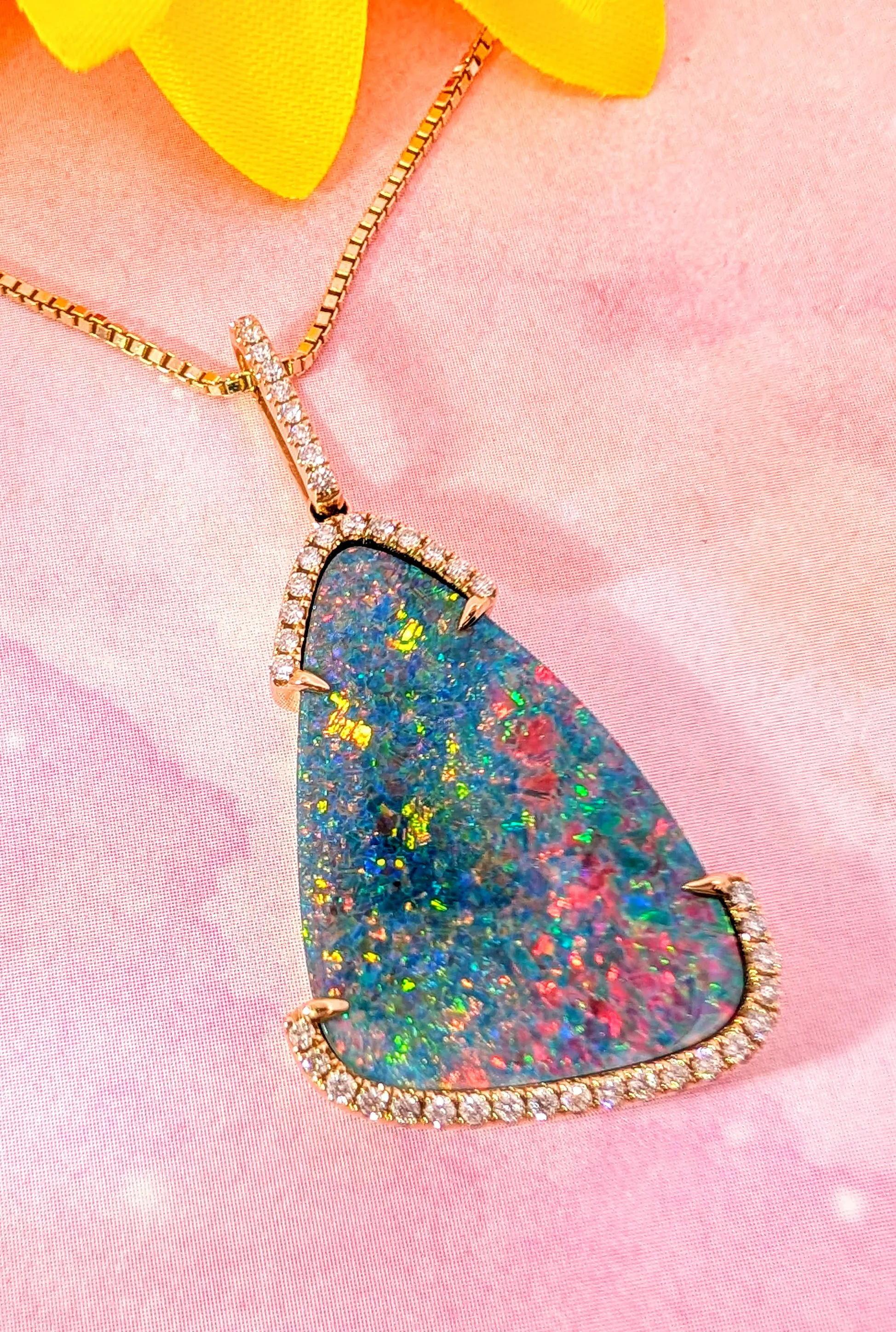 Opal pendant with diamond accents on a gold chain, set against a pink background. Visit Holly McHone Jewelers.