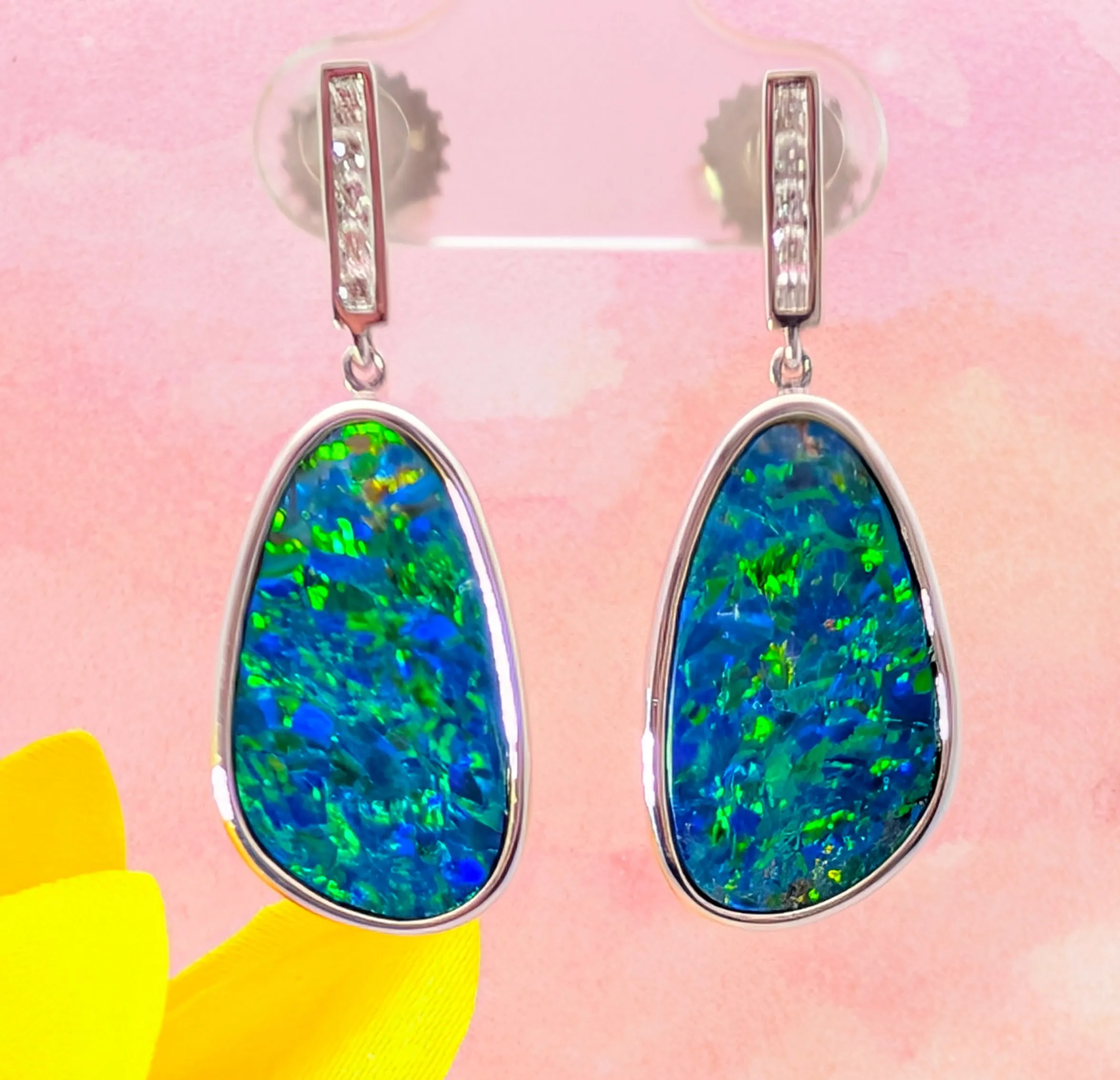 Blue and green opal earrings with diamond accents on a pink background.