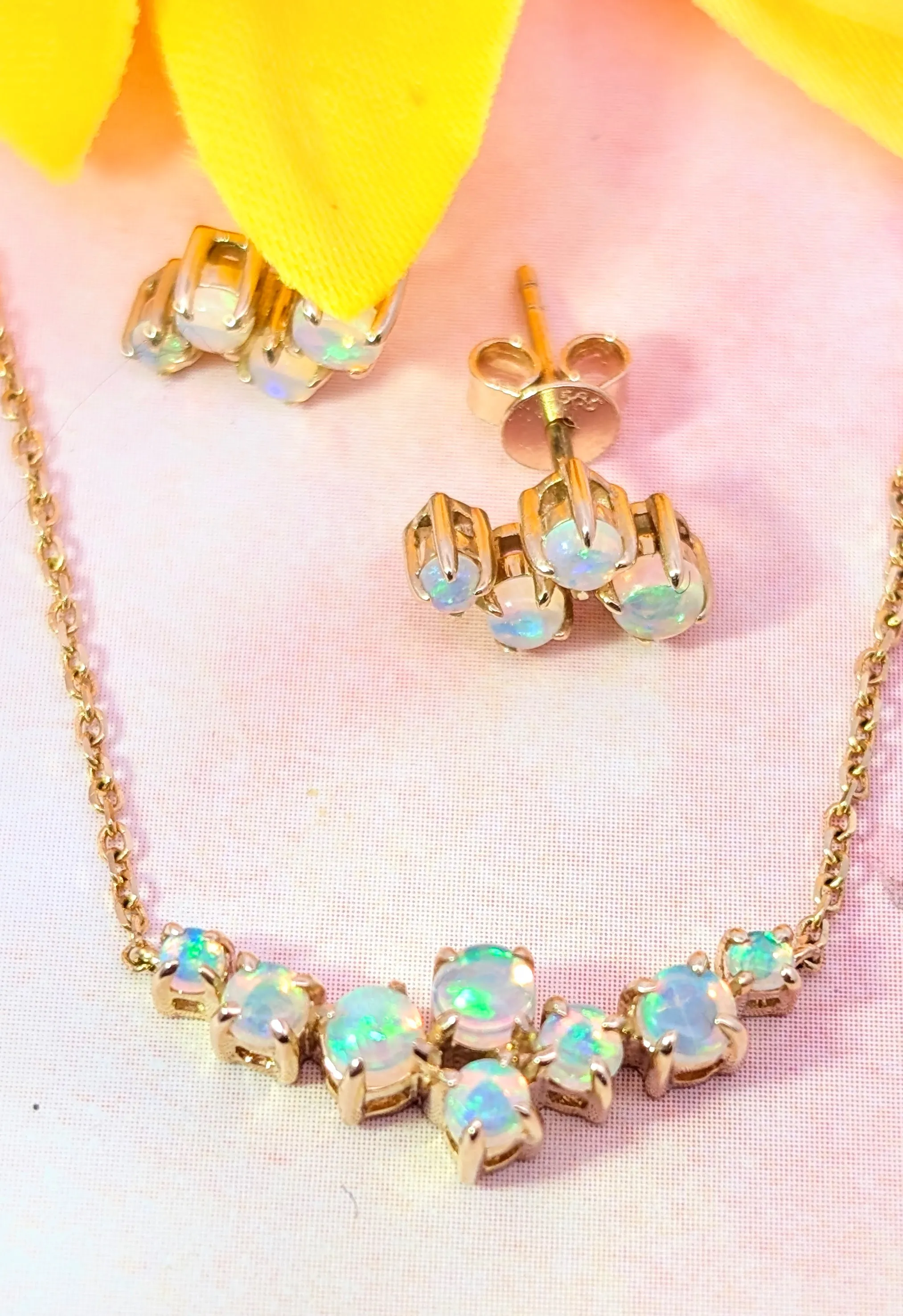 Opal necklace and earrings set with gold accents on a soft pink background.