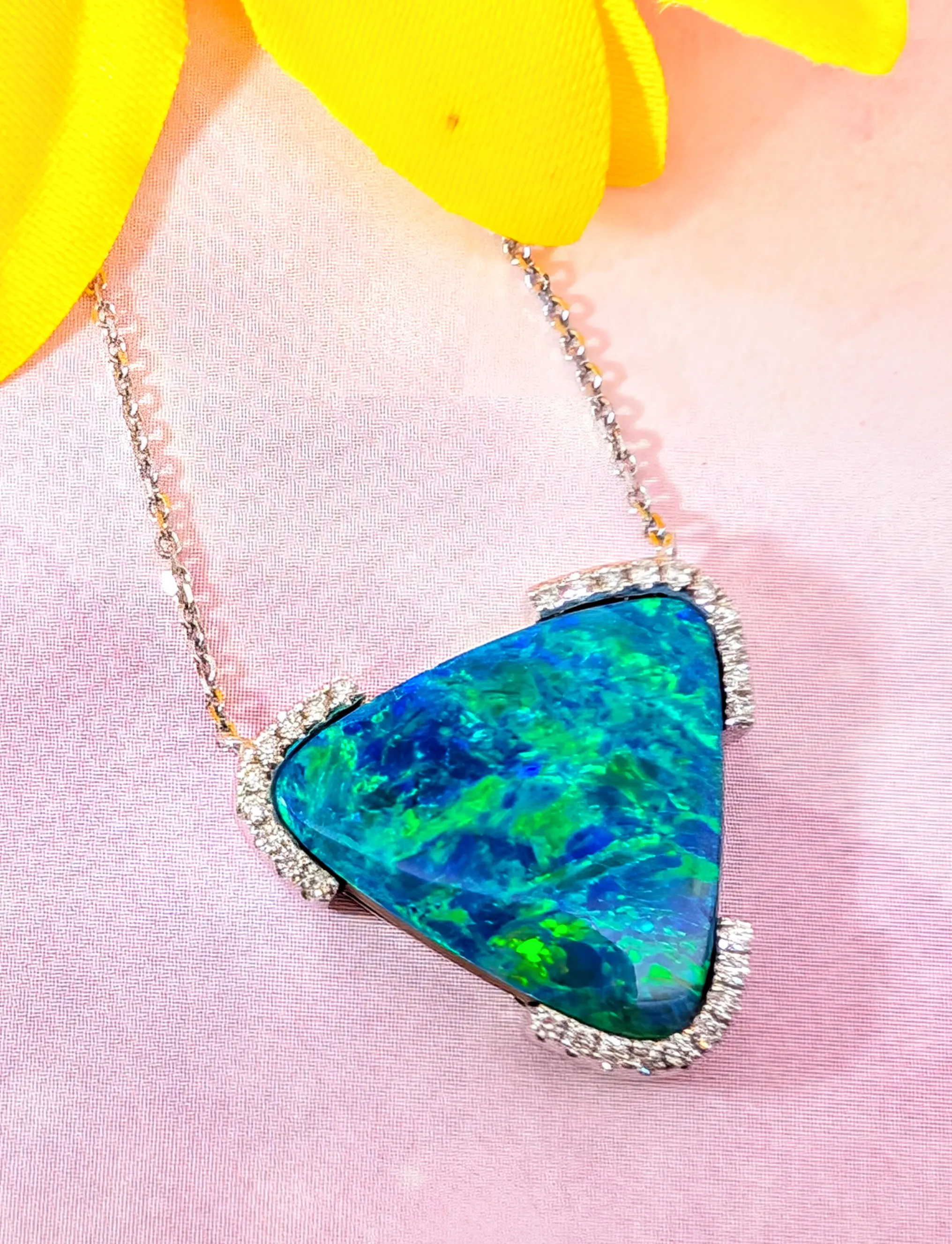 Triangular opal necklace with diamond accents on a pink background. Discover more at Holly McHone Jewelers.