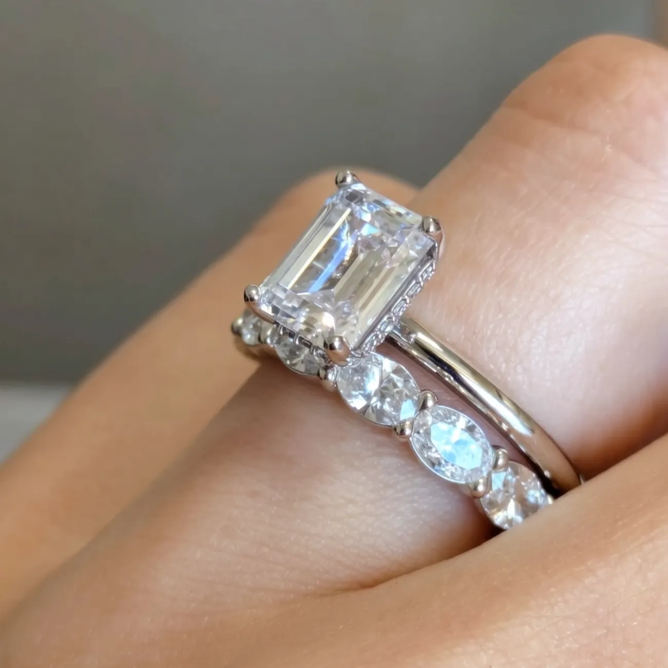 A hand wearing a large rectangular diamond ring with a silver band and accent stones.
