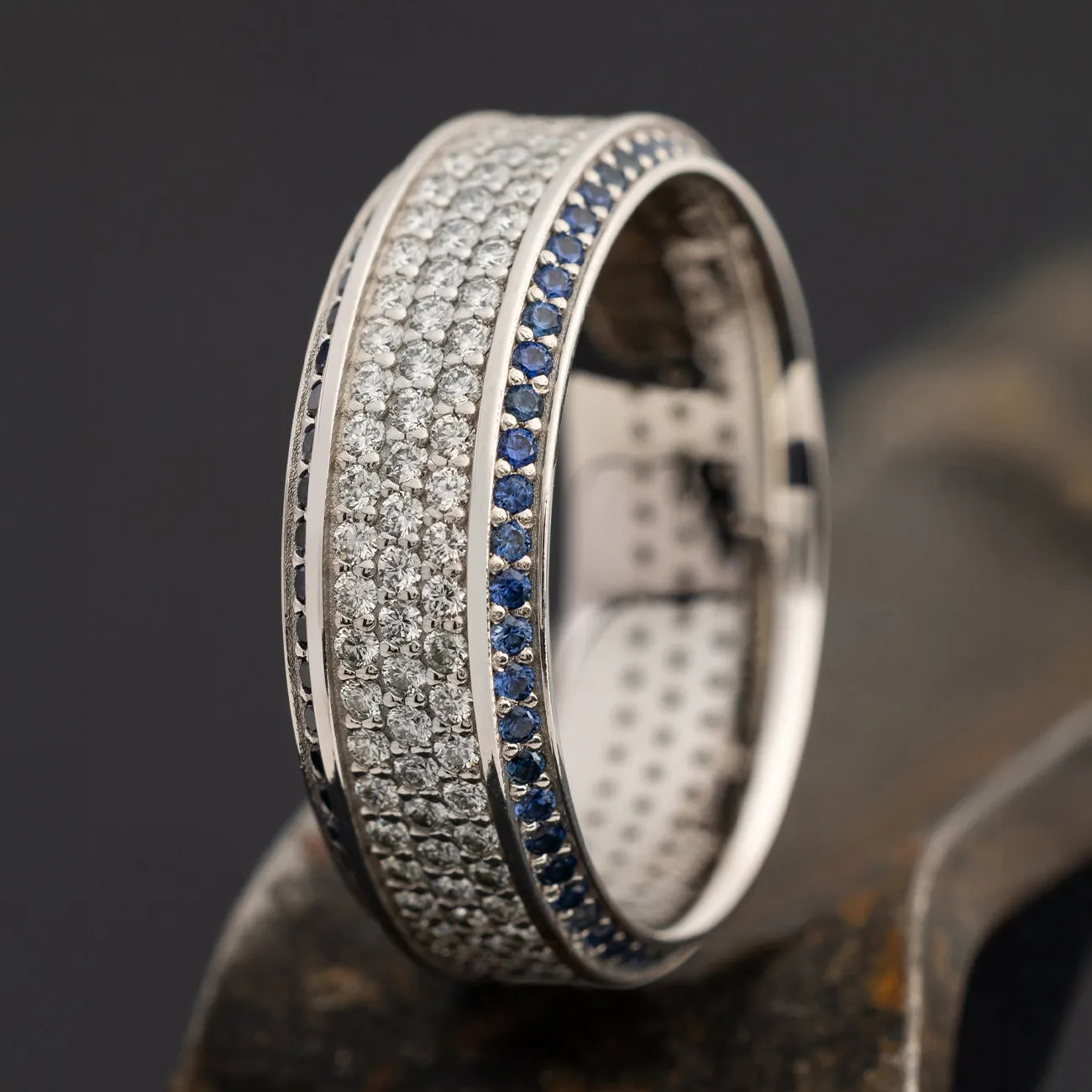 Men's wedding band with diamonds and blue stones on a dark background.