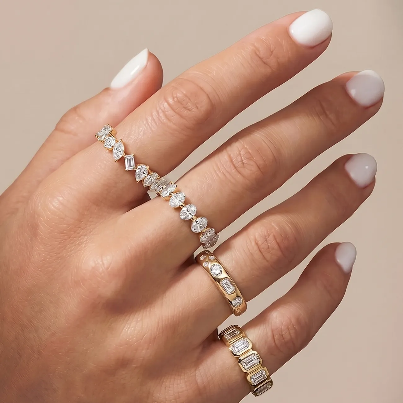 Hand with white nails wearing three gold rings with diamonds.