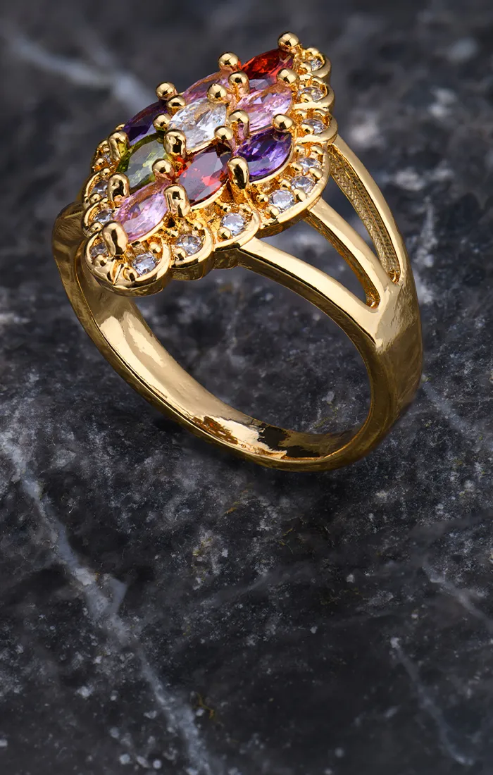 A gold ring with multicolored gemstones on a dark marble surface.