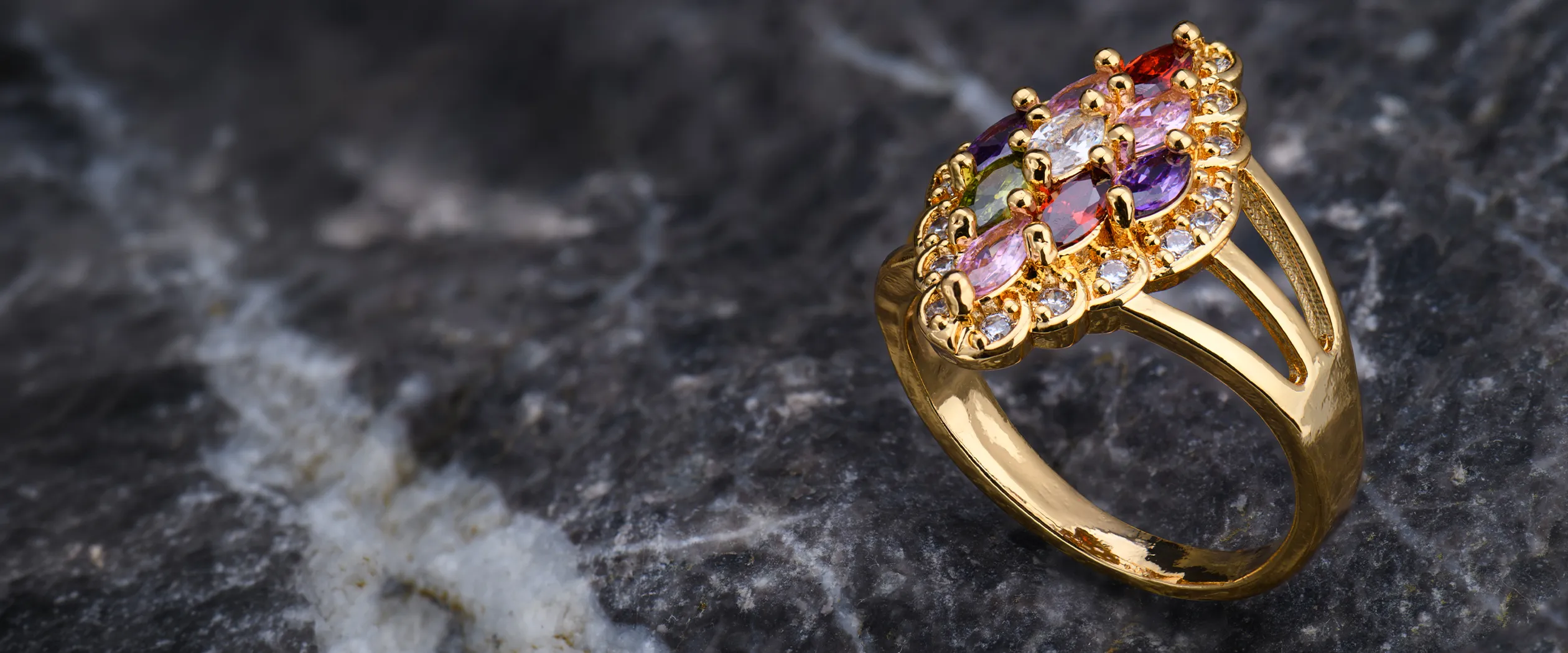A gold ring with multicolored gemstones on a dark marble surface.