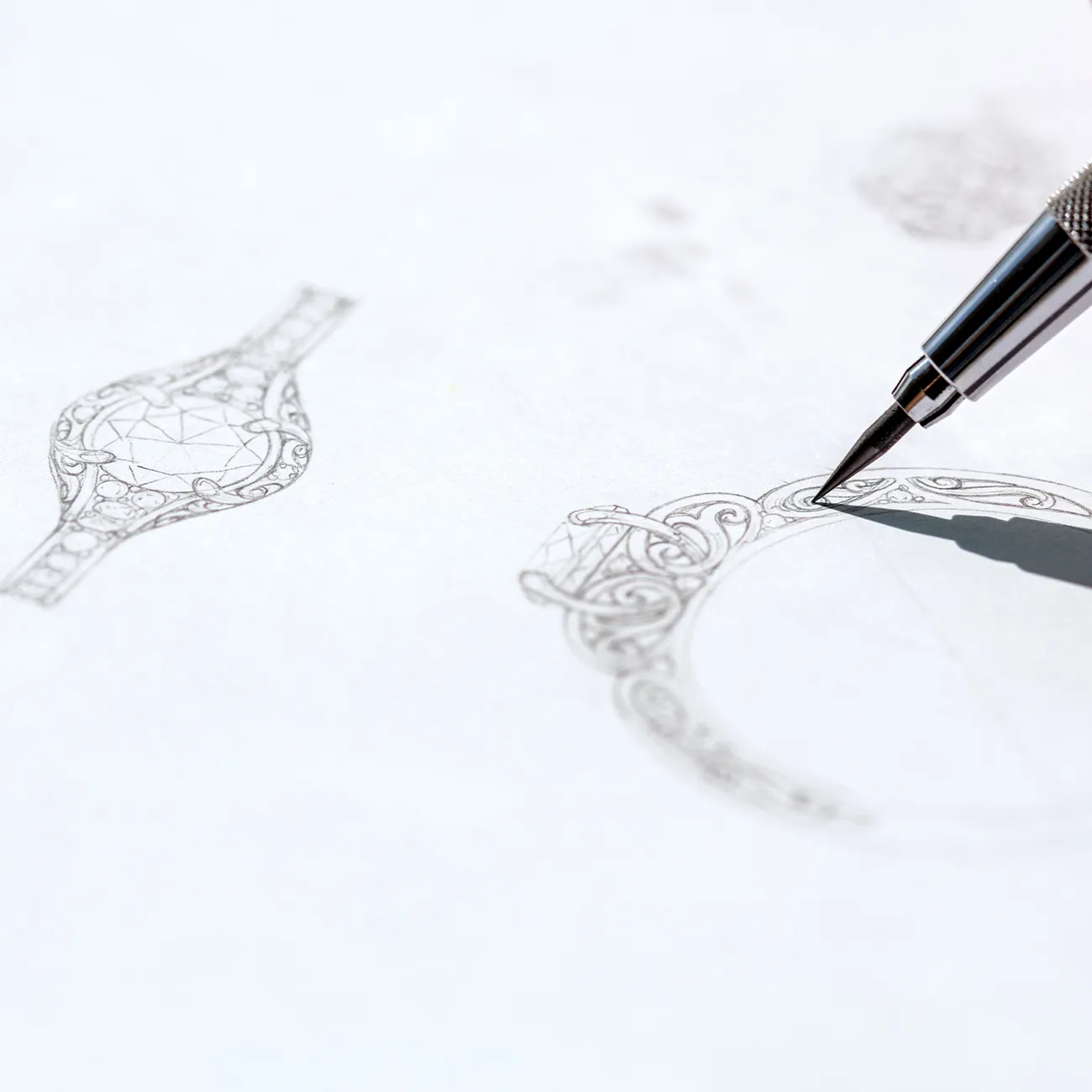 Hand sketching a detailed ring design with a large center stone and intricate patterns on paper.