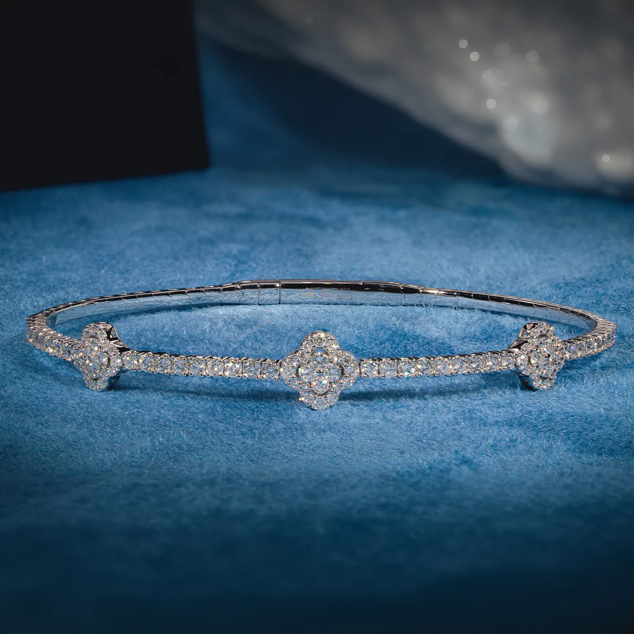 Elegant diamond bracelet with floral motifs on a blue surface.