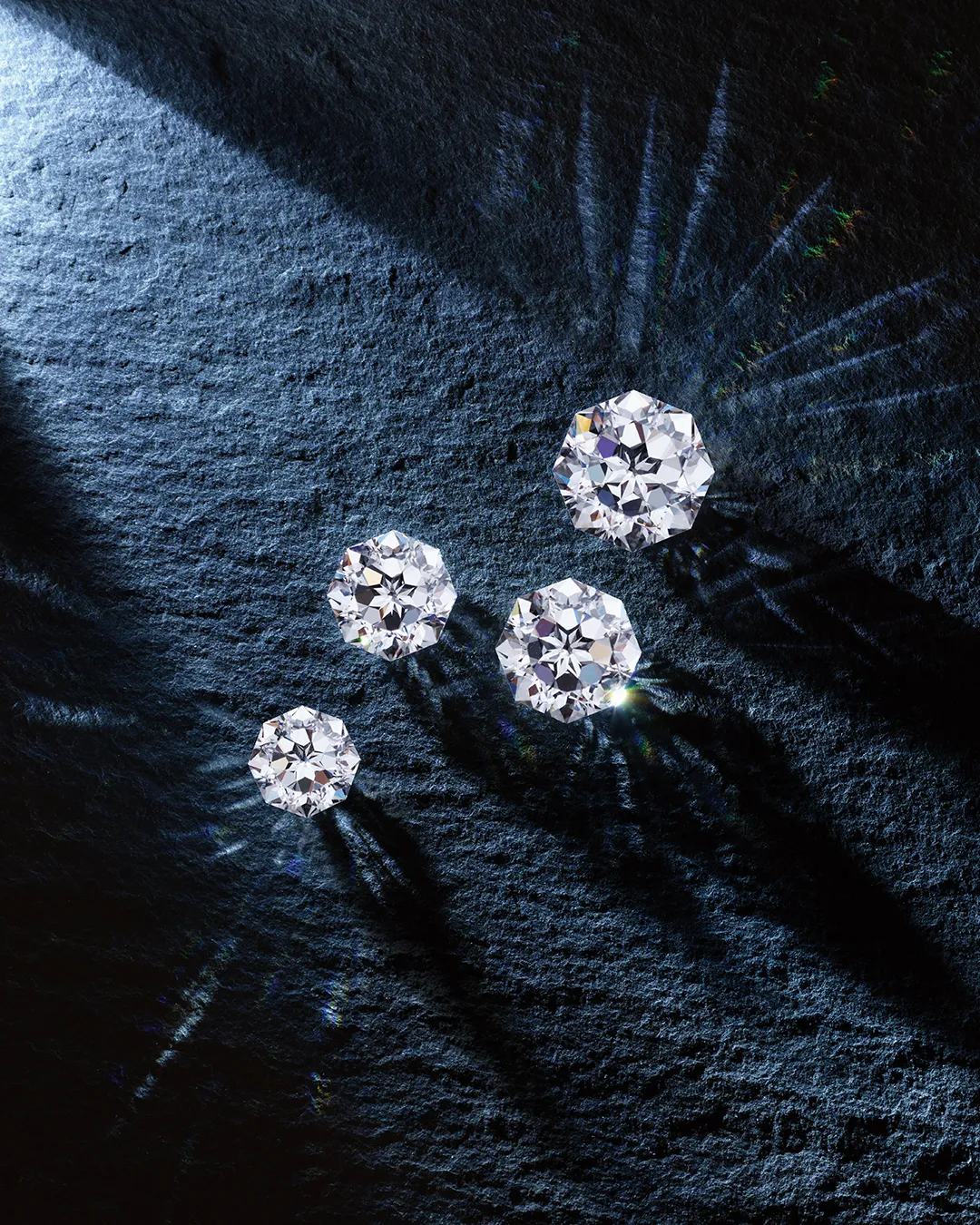 Four sparkling diamonds on a textured dark surface. Learn more about diamond buying.