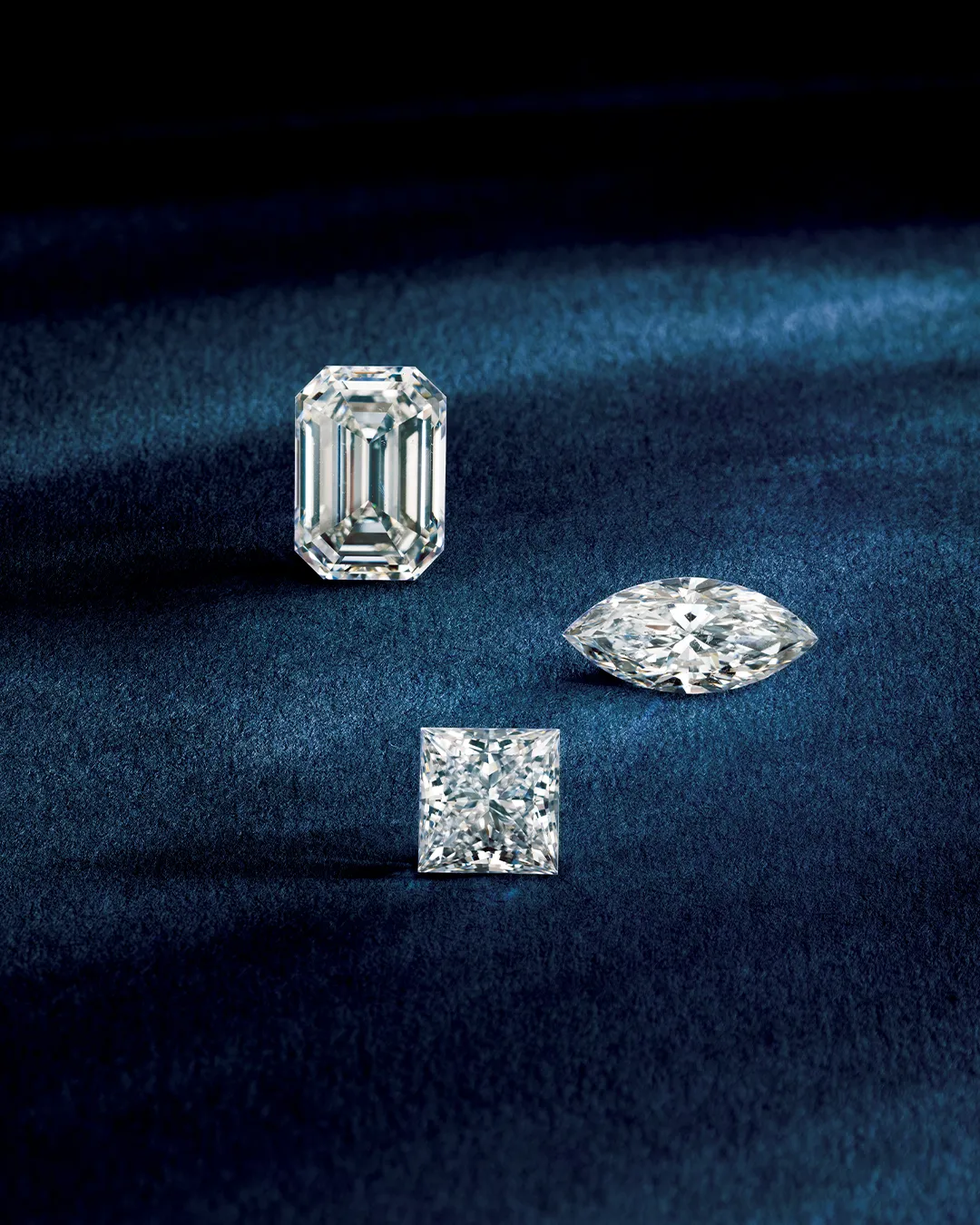 Three diamonds of different cuts on a dark blue surface. Learn more about lab-grown vs. natural diamonds.