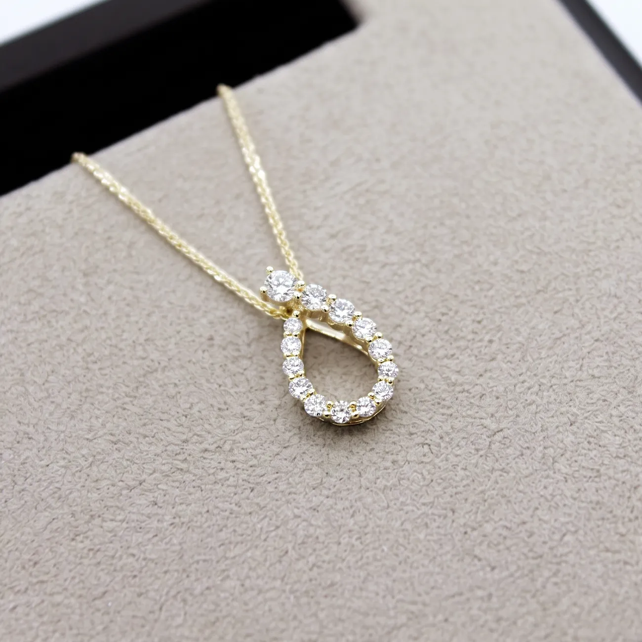 Gold necklace with a teardrop-shaped diamond pendant on a beige surface.
