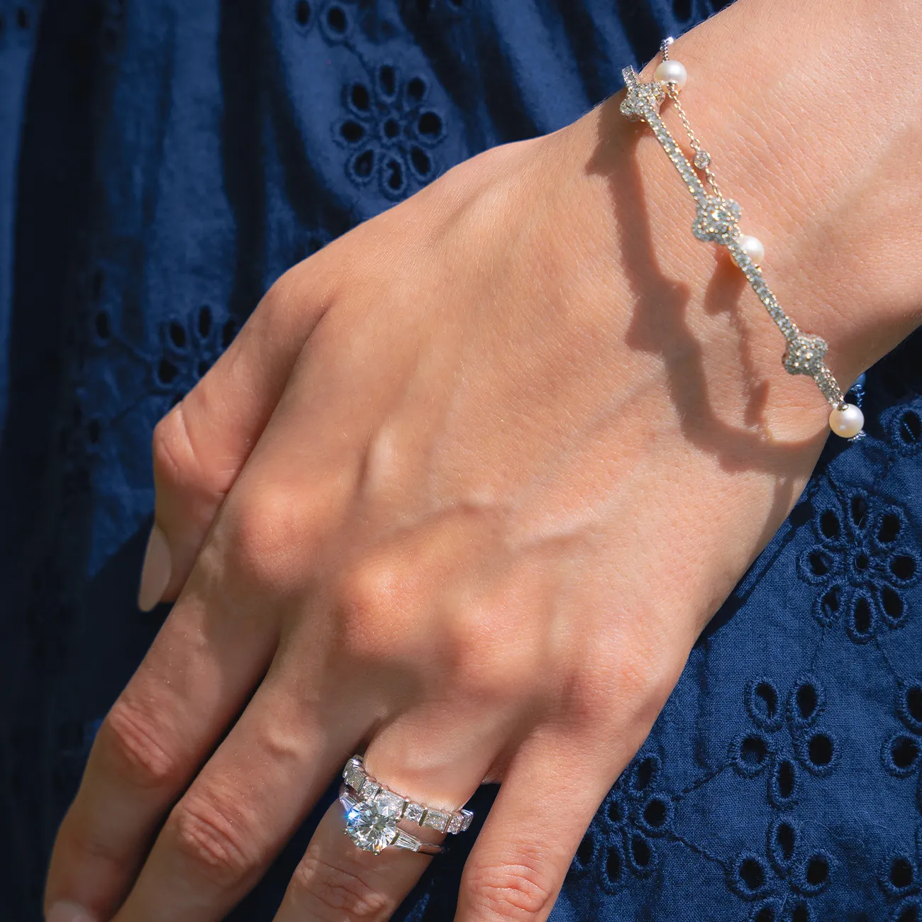 A hand wearing a diamond ring and a delicate bracelet with pearls and star shapes.