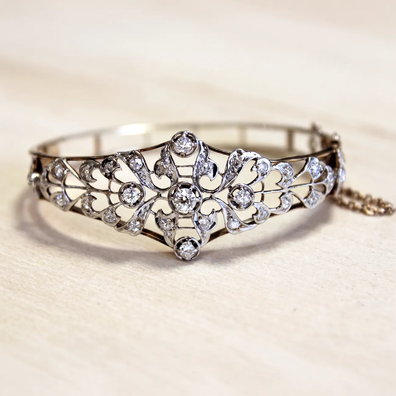 An ornate silver bracelet with intricate filigree and diamond accents on a light background.