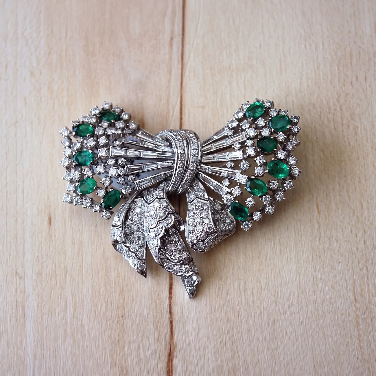 Elegant silver brooch with emerald and diamond accents on a wooden surface.